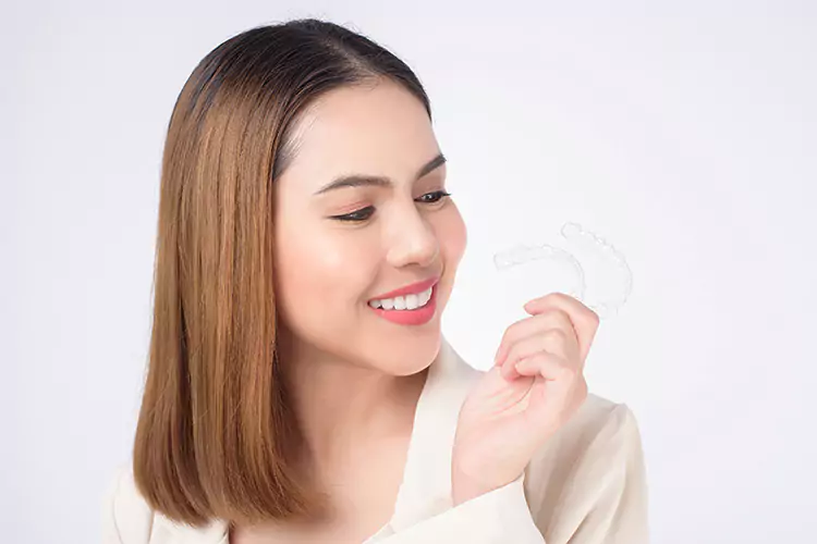 Smiling woman holding two Invisalign clear aligners