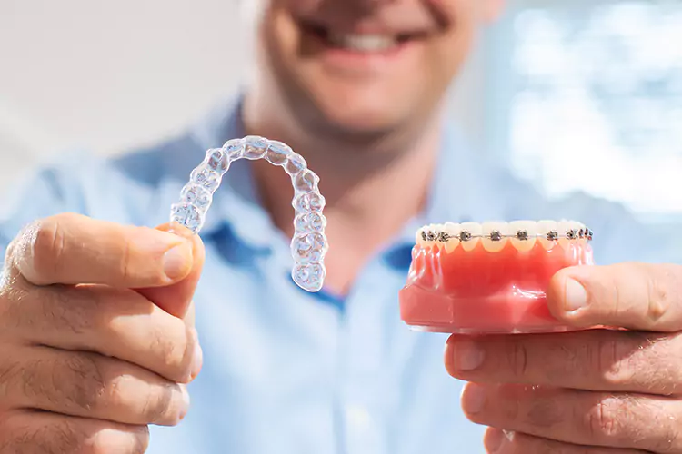 Man holding Invisalign in one hand and dental model with braces in the other hand