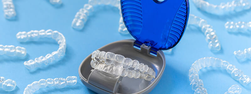 Invisalign clear aligners in a storage case, with more Invisalign clear aligners scattered around
