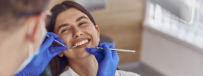 Dentist examining a smiling patient with dental tools