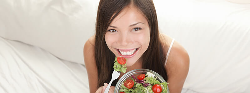 Smiling woman eating salad with tomatoes